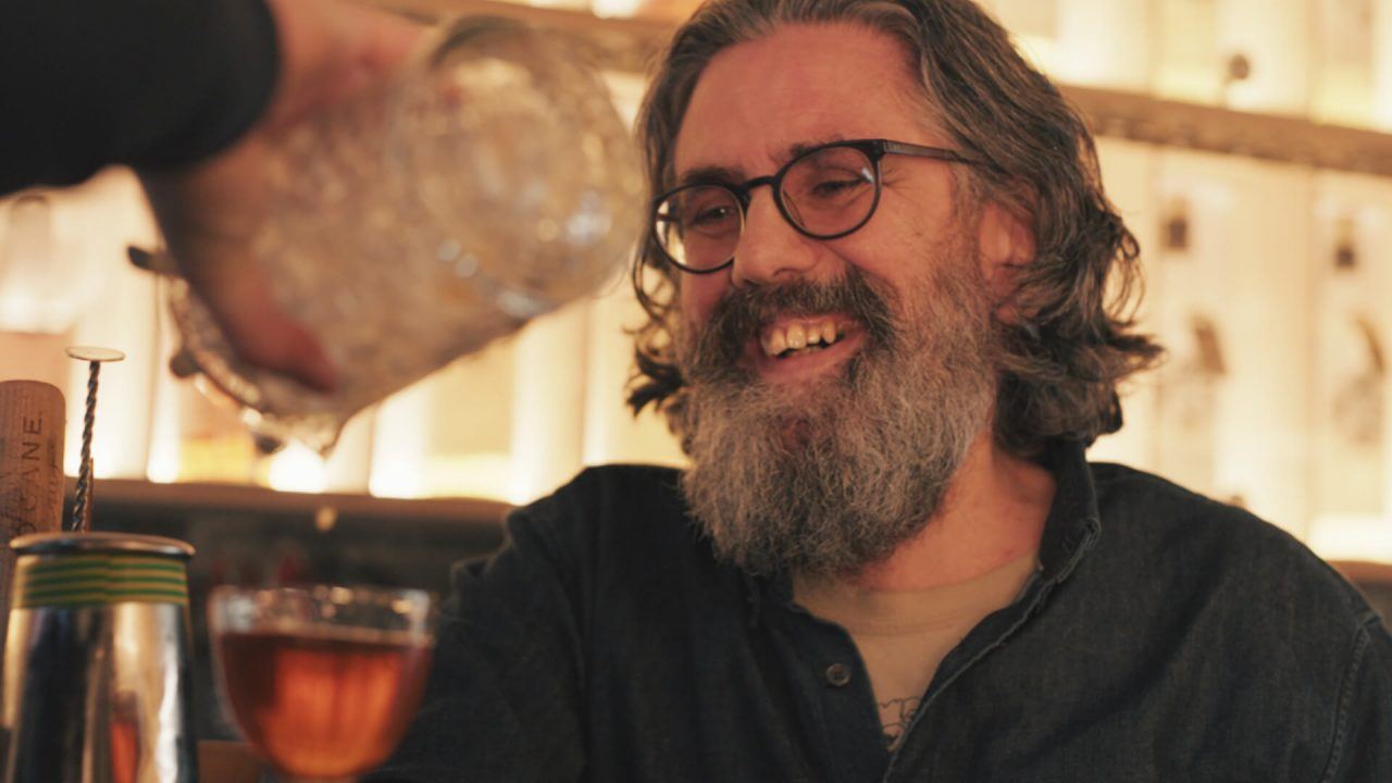 A man smiling with a bar behind him