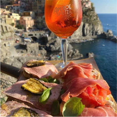 An image of an Aperol Spritz glass with the coast of Italy at the background