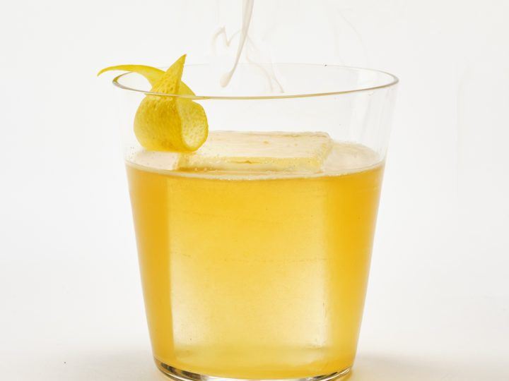 An Longbranch cocktail, on the rocks, against a white background with a whisp of smoke.