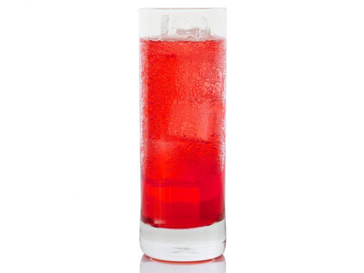 A Campari Soda in a sweating highball glass, sits on a white backdrop.