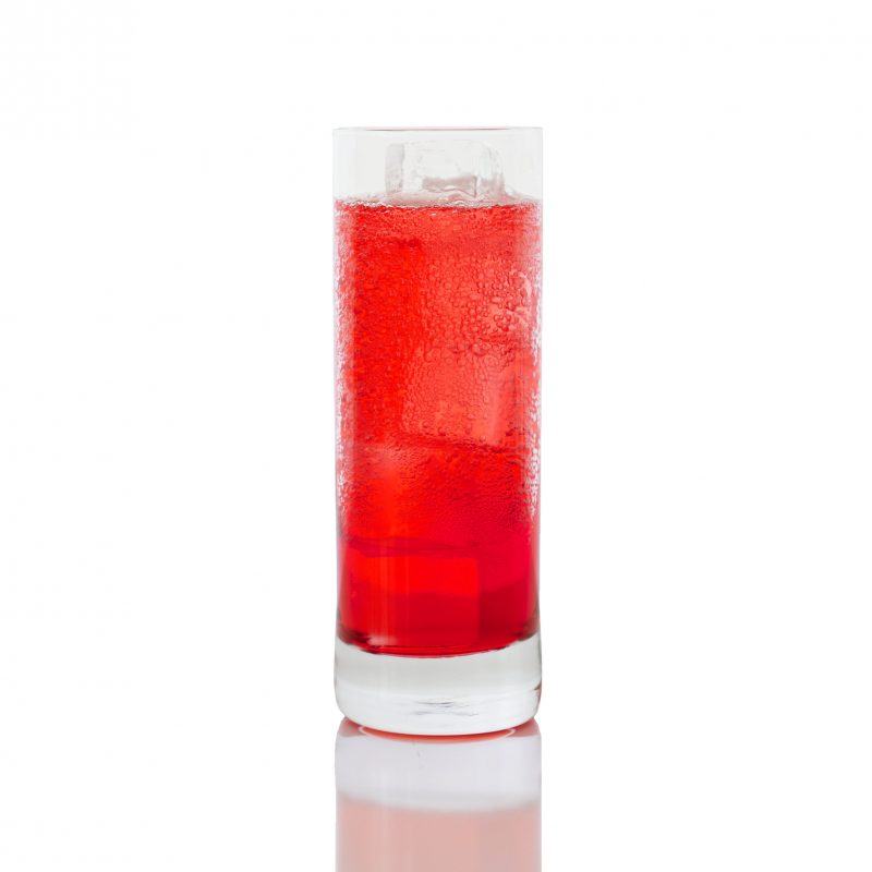 A Campari Soda in a sweating highball glass, sits on a white backdrop.