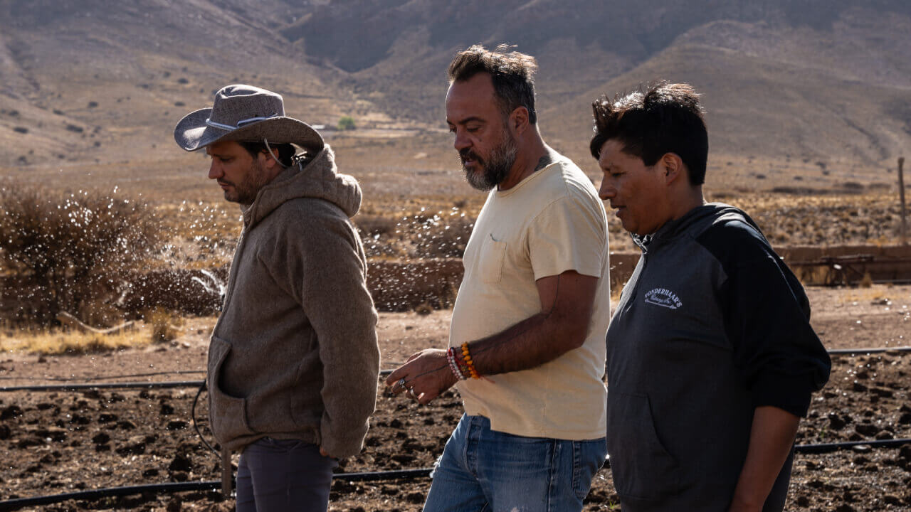 Three men sitting on chairs in the middle of an arid landscape