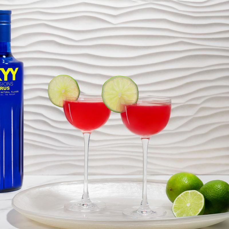 Dos copas de Cosmopolitan, que es un cóctel rojizo. A su lado, una botella de Skyy Vodka.