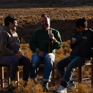 Three men sitting on chairs in the middle of an arid landscape